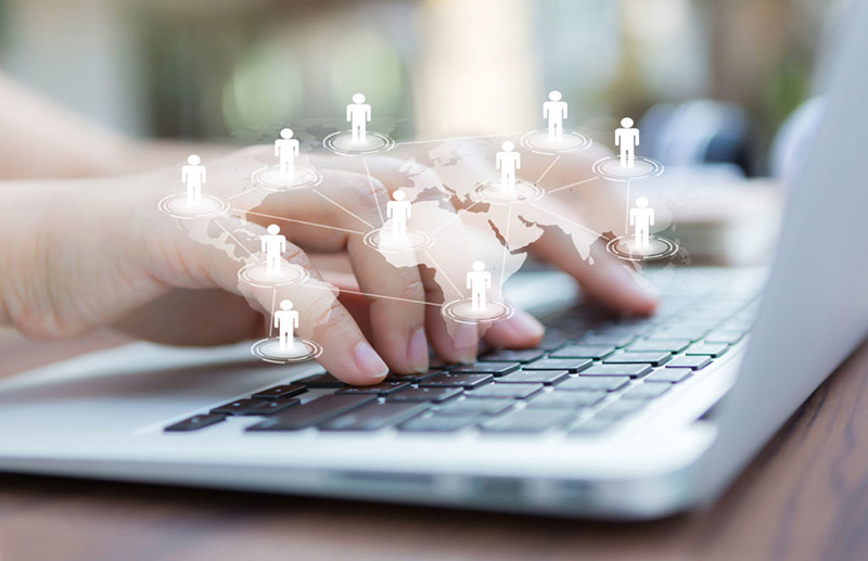 A hand is typing on the lap top and a figure of a network of people is shown on that hand which indicates recruitment