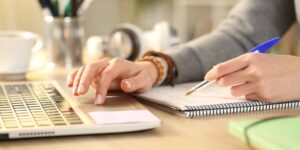 hand typing on a laptop and writing notes